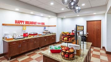 Un espace réservé au petit-déjeuner, avec une pancarte indiquant : « C’EST ICI QUE COMMENCE UN PETIT-DÉJEUNER JOYEUX ». On y trouve divers aliments et un panier de fruits sur le comptoir.