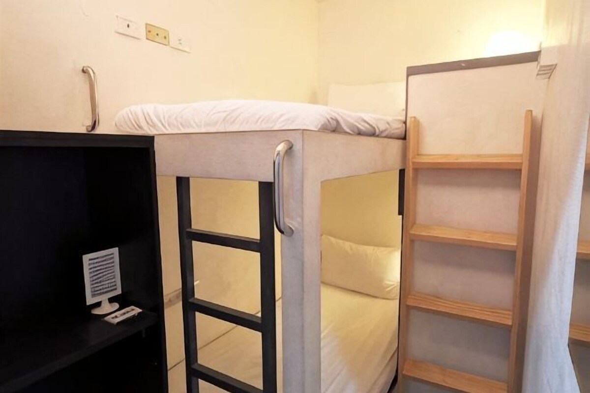 A bunk bed with a ladder, a shelf unit, and a power outlet on the wall.