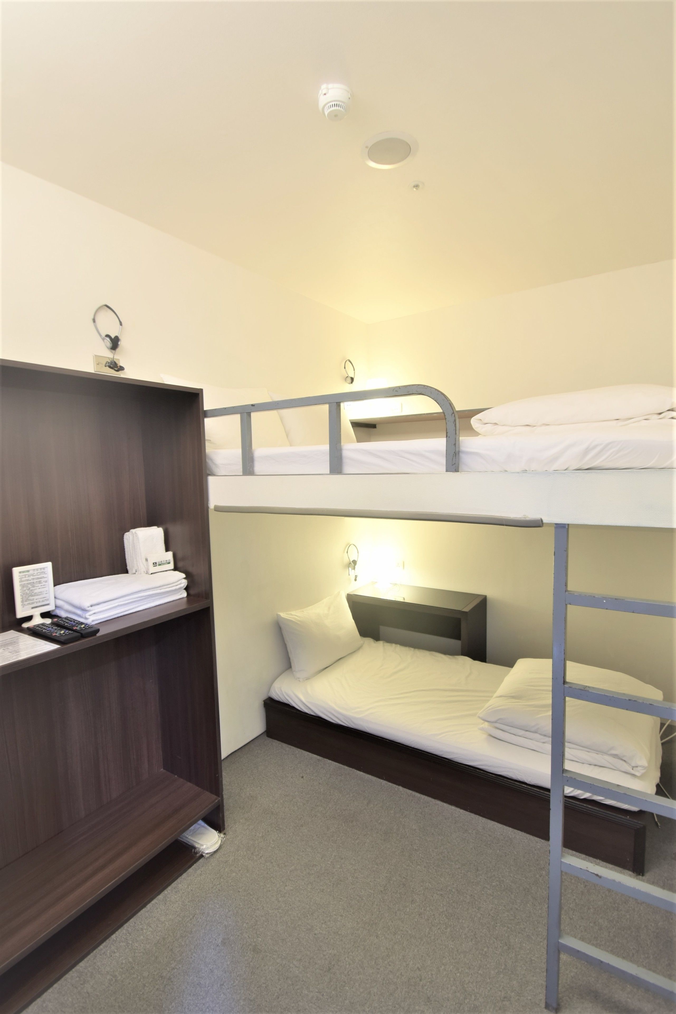 A bunk bed room with a desk and shelves, a bedside lamp, and a ceiling light.