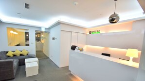 A modern hotel lobby with a reception desk, a sofa with yellow cushions, and a minimalist design. - Inn Cube Ximen (Taipei)