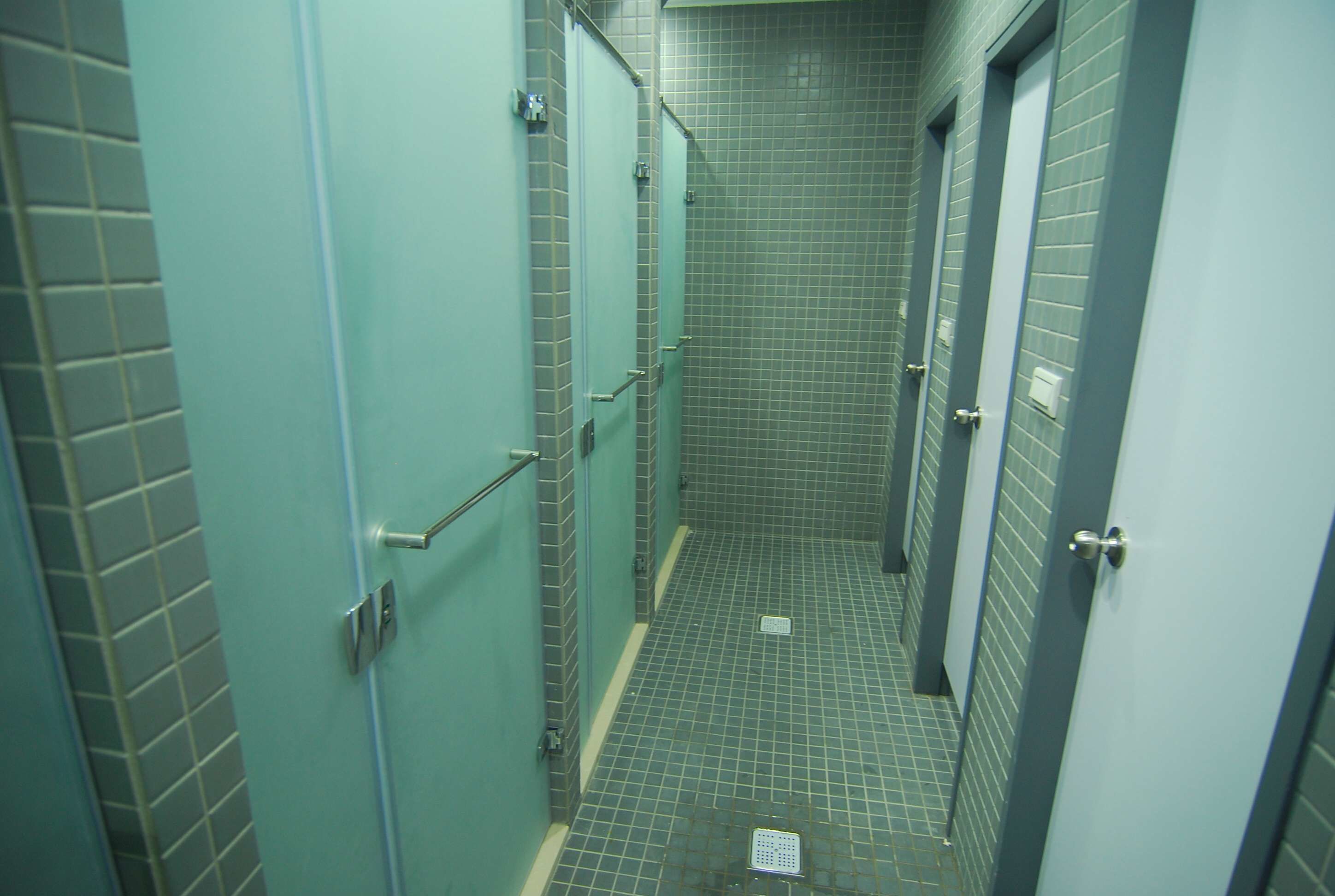 Un pasillo estrecho con paredes de azulejos y puertas, que da acceso a cabinas individuales.