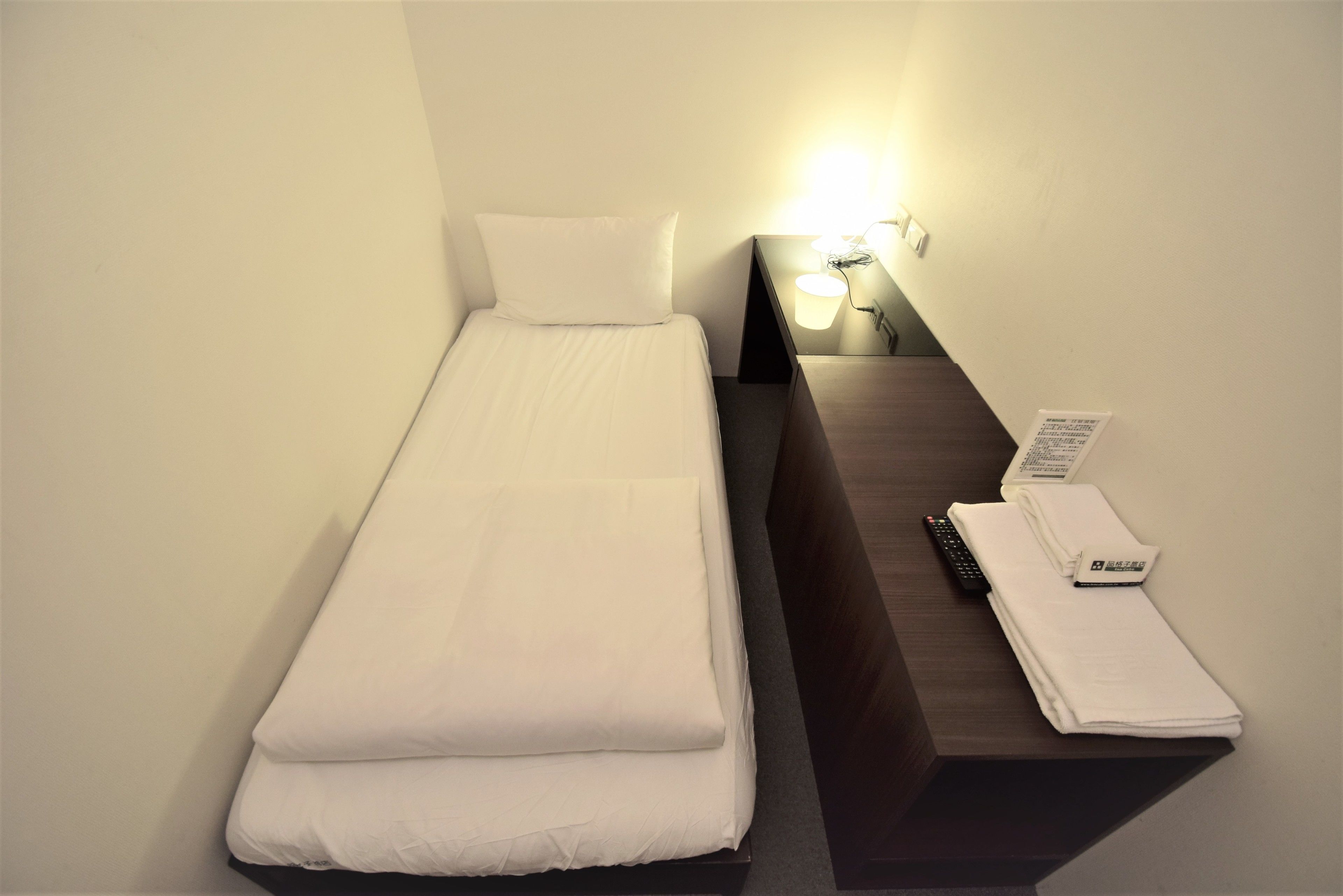 A single bed with white bedding, a bedside table with a lamp, and a telephone.