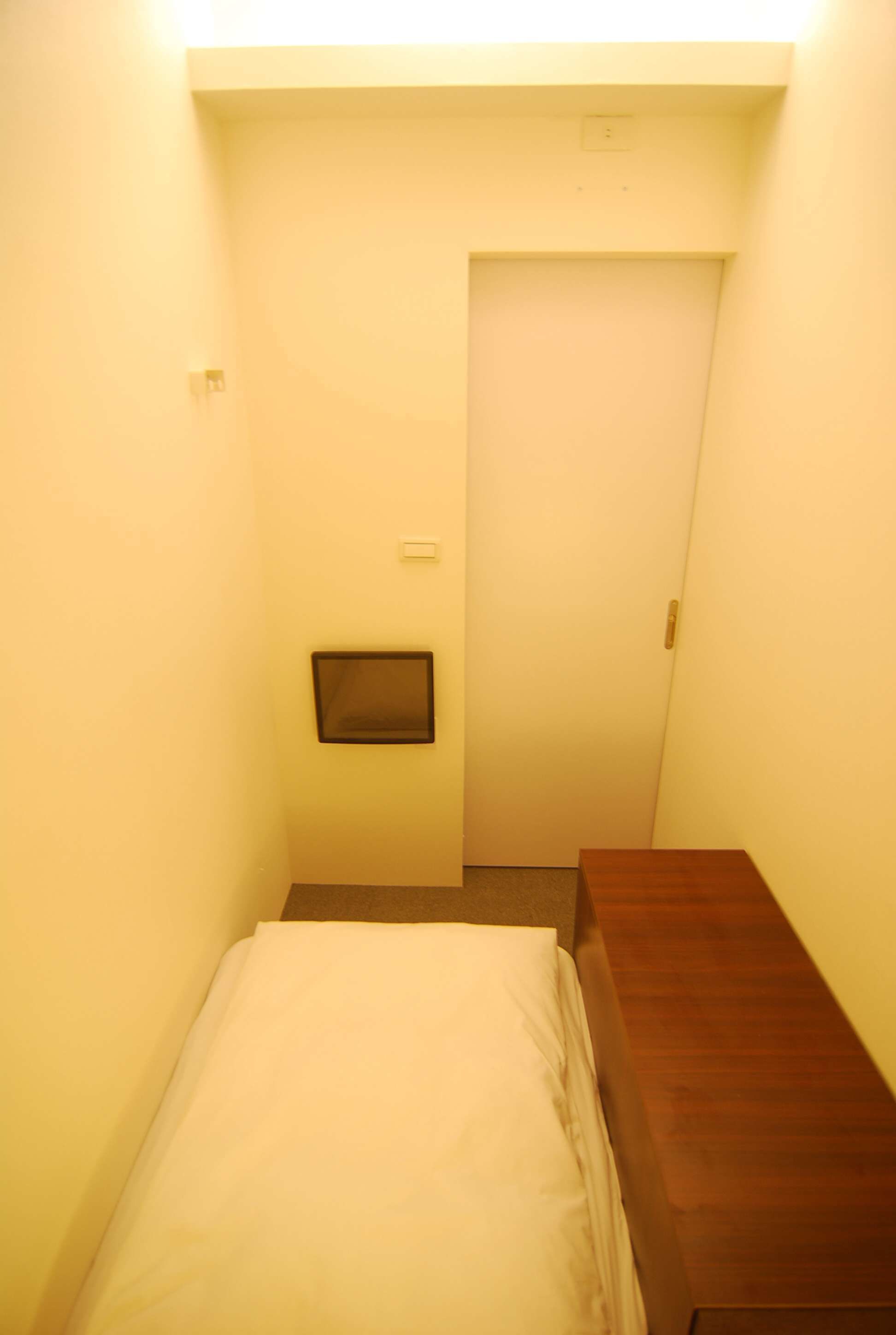 A narrow hallway with a bed on the left and a wooden bench on the right.