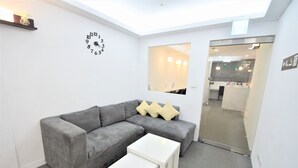 A modern living room with a grey sectional sofa, a white coffee table, and a wall clock. - Inn Cube Ximen (Taipei)