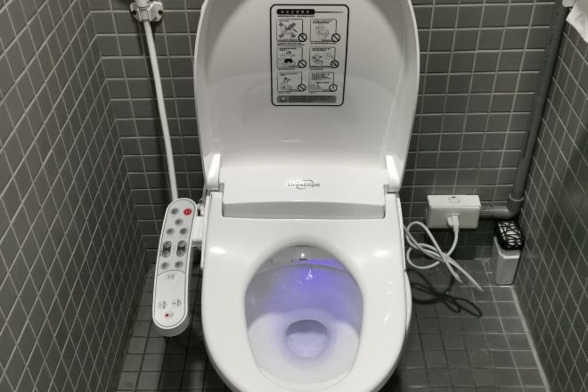 A modern toilet with a control panel and a foot pedal, set in a tiled bathroom.