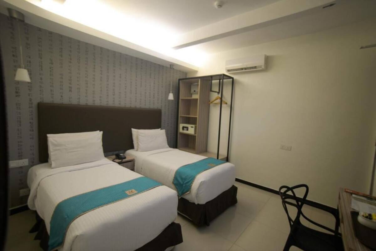 Habitación de hotel con dos camas, un armario, un escritorio y una silla.