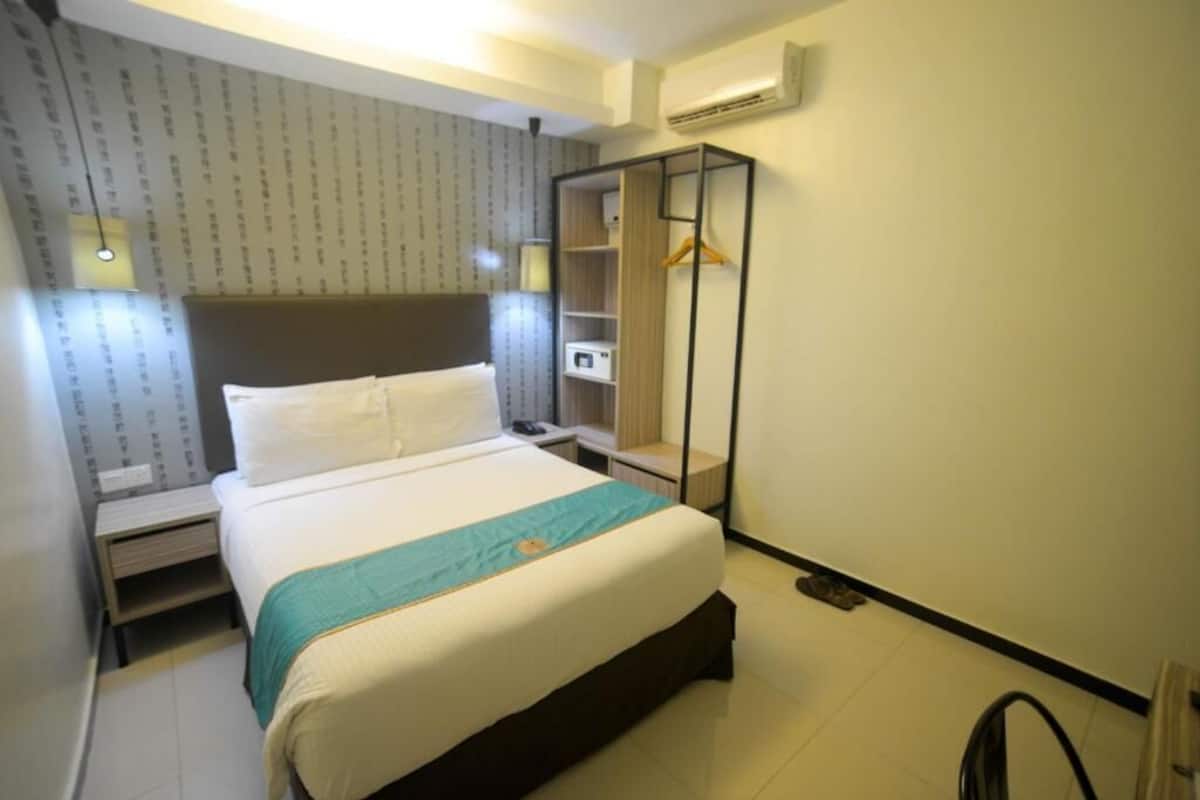 Una habitación de hotel con cama, mesita de noche, armario y perchero.