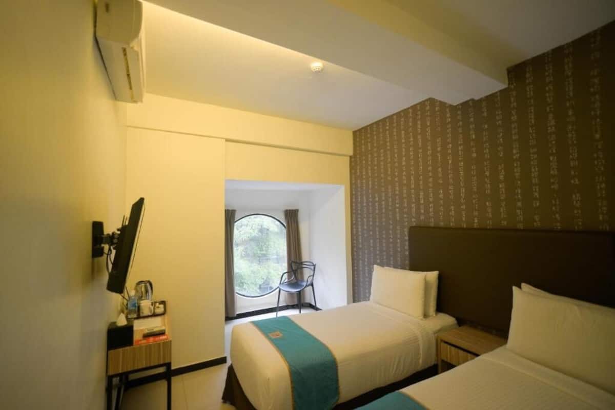 Habitación de hotel con dos camas, un escritorio con silla, ventana con vistas y televisor instalado en la pared.