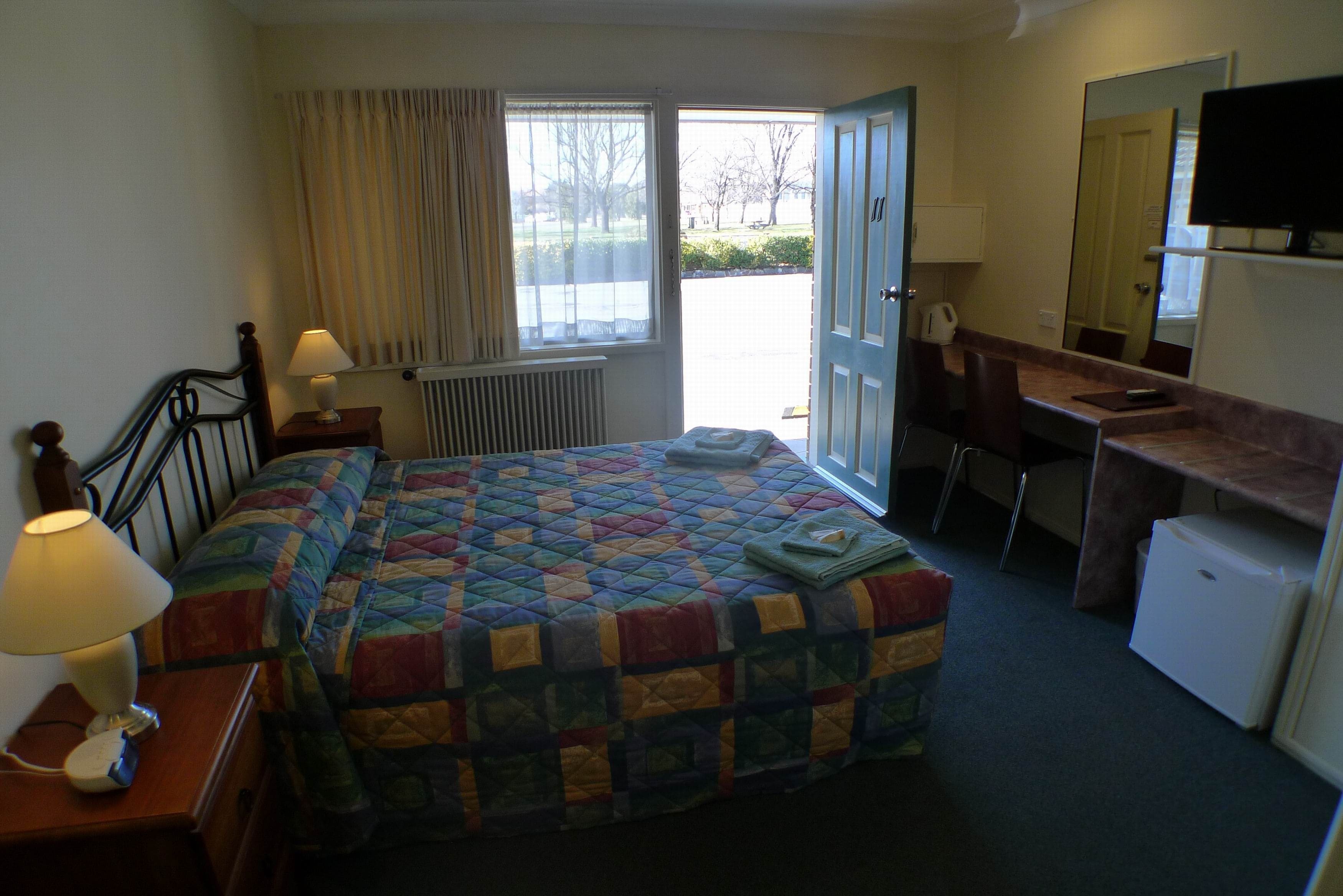 Una habitación de hotel con cama, escritorio, silla, televisor y ventana con cortinas.