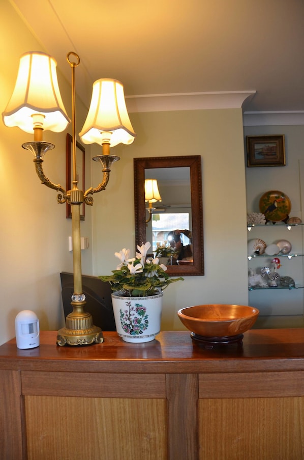 A wooden cabinet with a white device, a brass lamp, a potted plant, and a ceramic bowl.