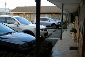 A parking area with several cars parked in front of a building with a tiled roof and a covered walkway.