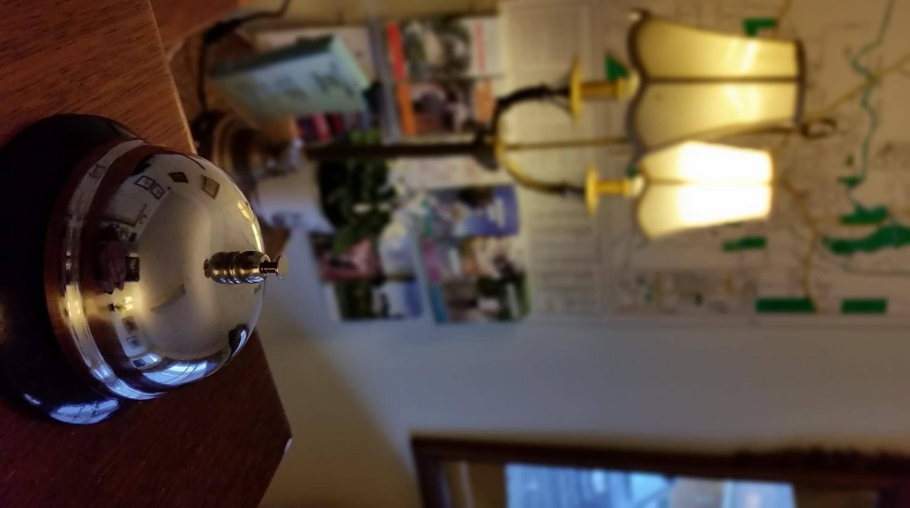 Una habitación con una lámpara de escritorio, un reloj y una pared decorada con varios papeles y fotografías.
