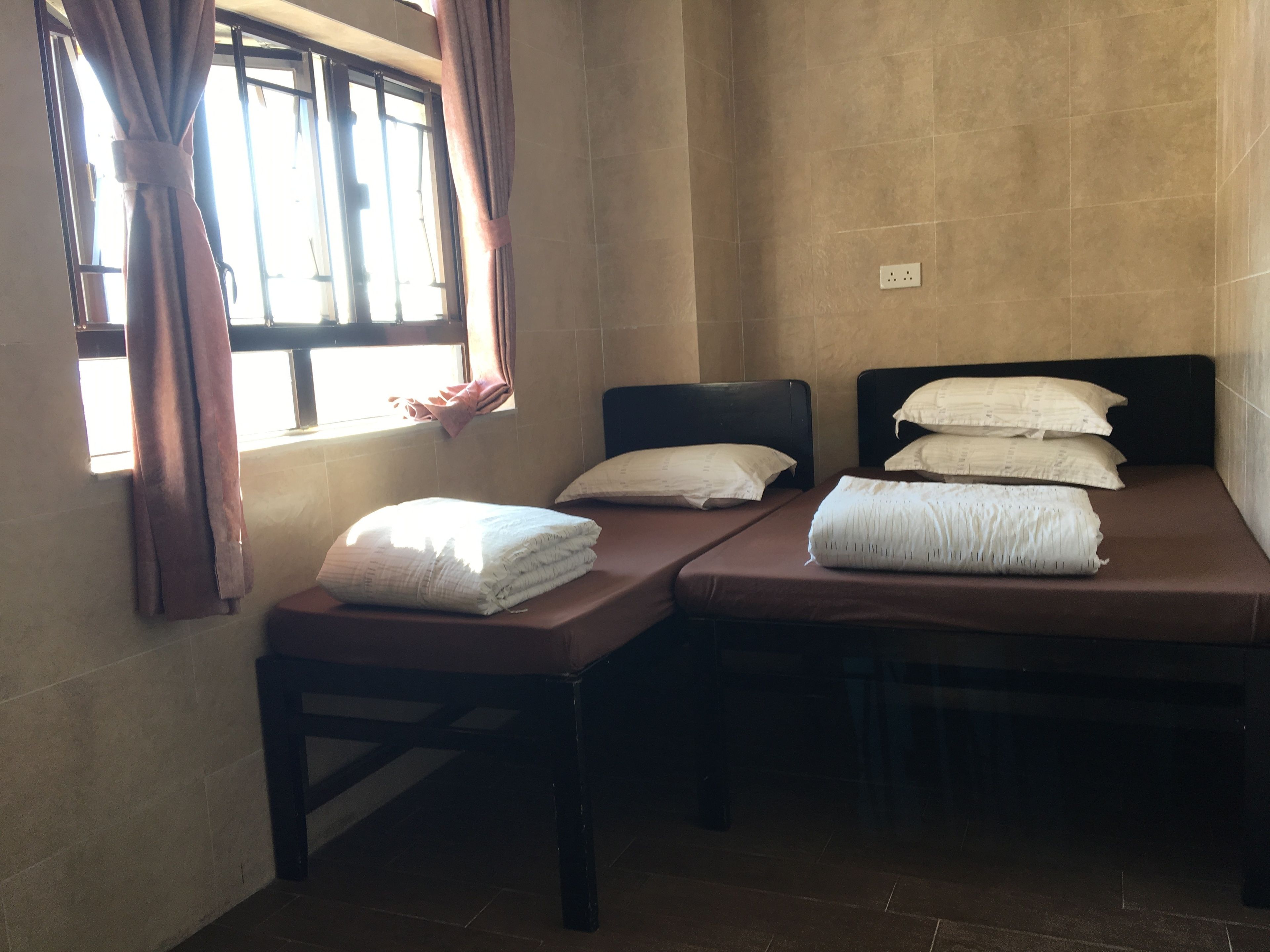 A room with two single beds, a window with curtains, and a tiled wall.