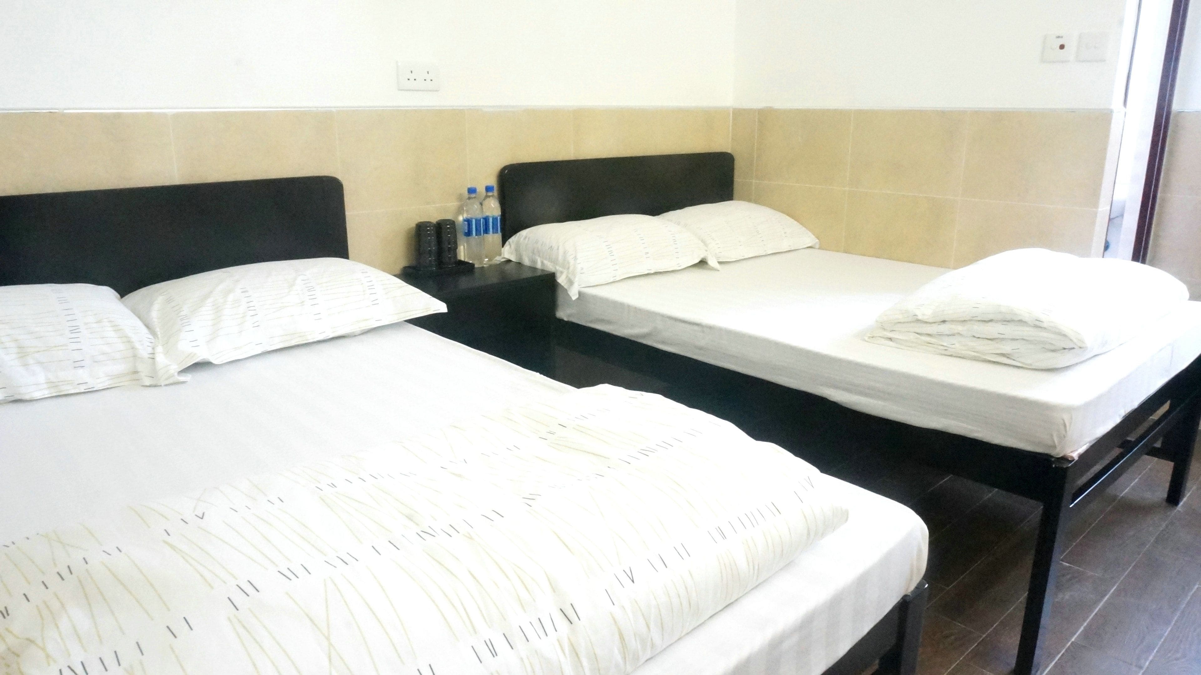 Two single beds with black headboards, white linens, and a small table with a bottle and remote controls between them.