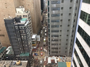 Un edificio de gran altura con varios pisos, una calle estrecha entre los edificios y algunos vehículos estacionados.
