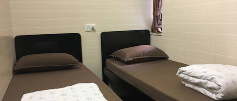 A small, single-room accommodation with two single beds, each with a pillow and a blanket.