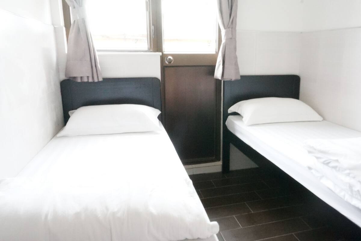 Una habitación con dos camas individuales, una ventana con cortinas y un radiador.