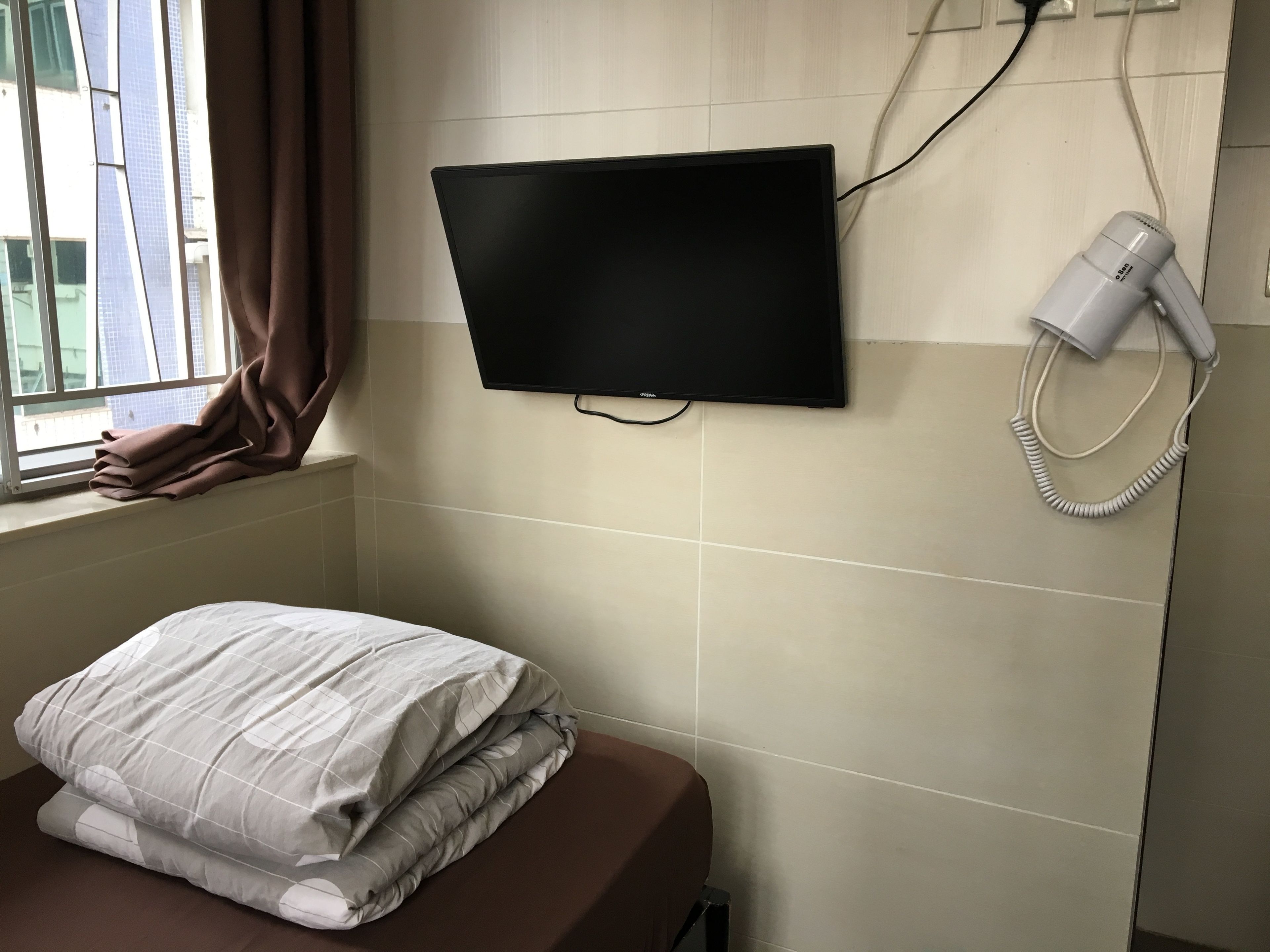 A hotel room with a bed, a TV mounted on the wall, and a hairdryer plugged in.