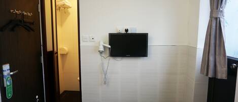 A hotel room with a bed, a bathroom with a shower, a mounted TV, and a hairdryer.