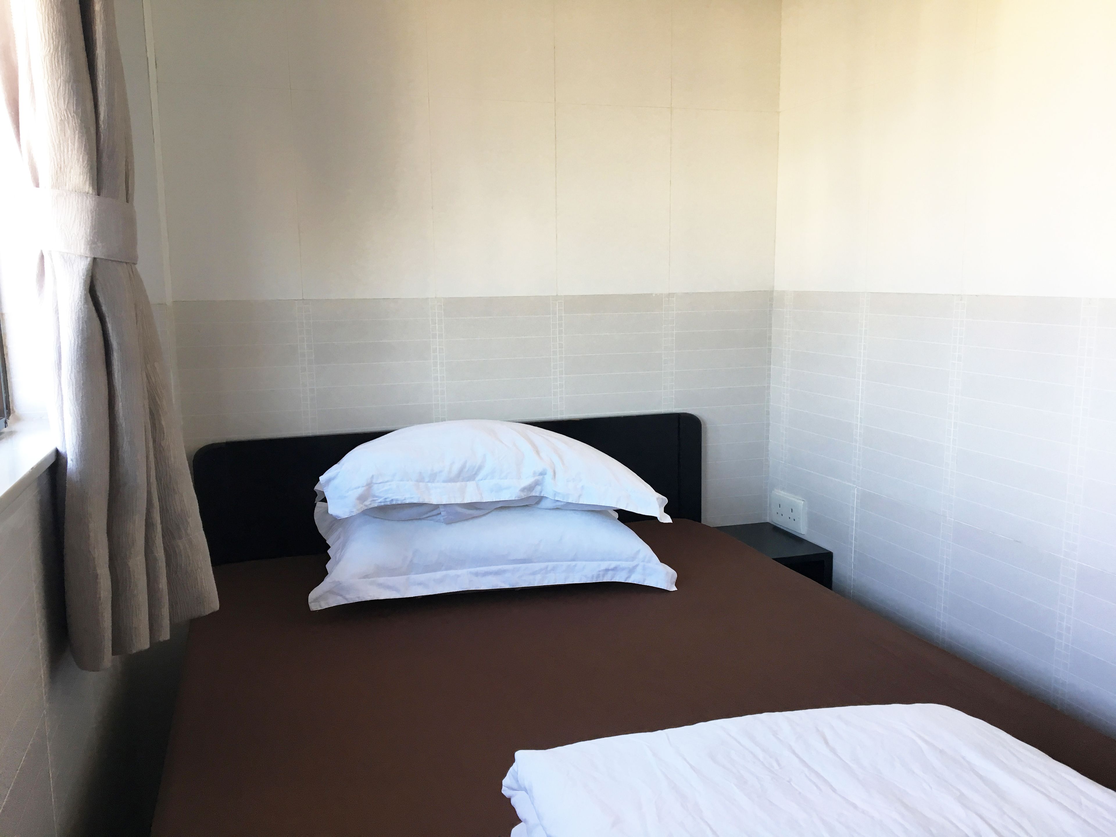 Una cama individual con dos almohadas y una colcha marrón en una habitación con paredes de baldosas blancas.