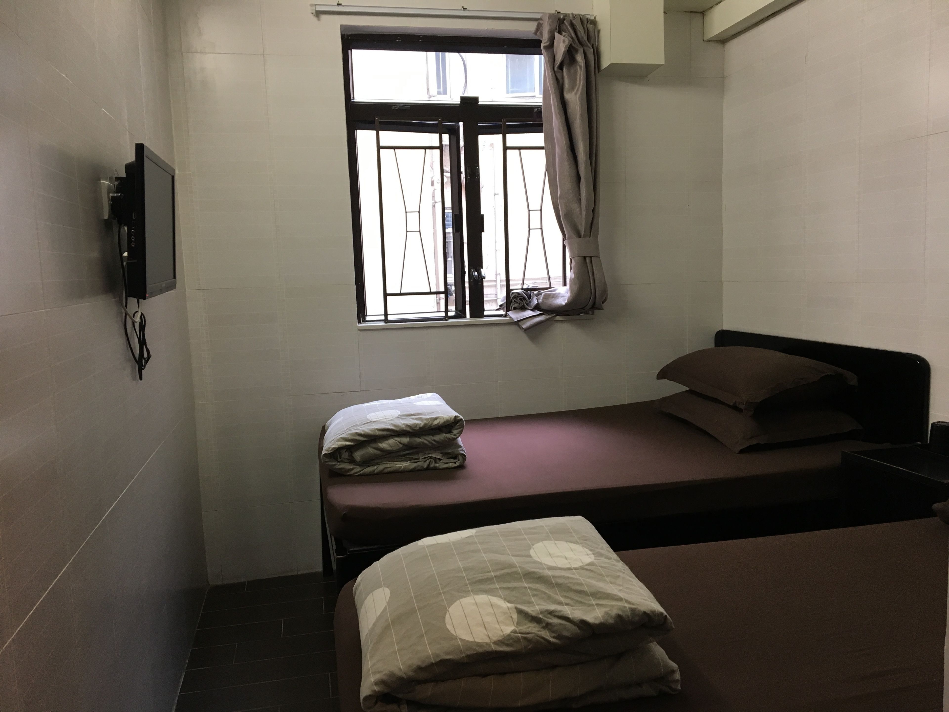 A small, single-bed room with a window, a TV mounted on the wall, and a curtain.