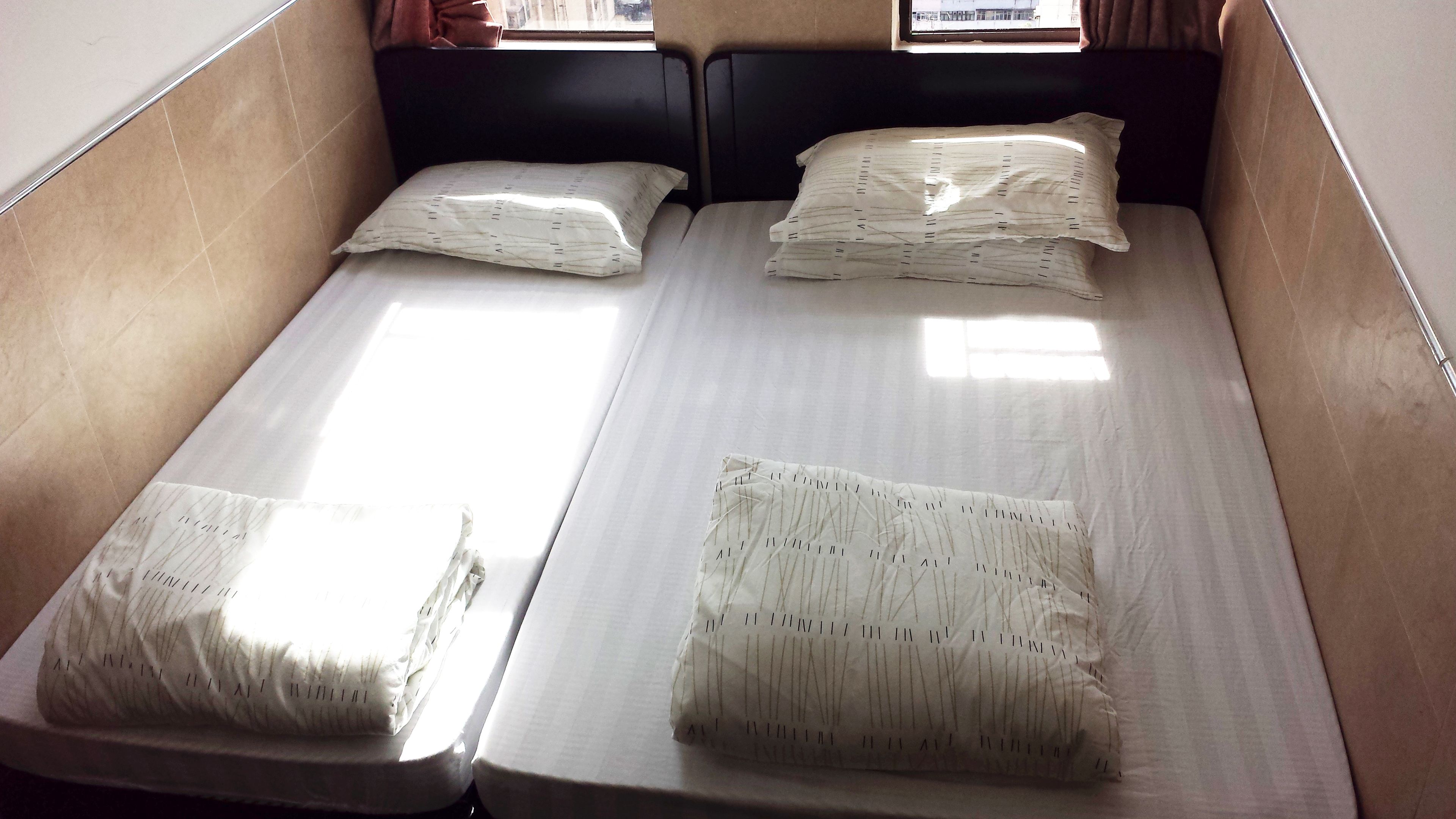 A single bed with a mattress and pillows, a headboard, and a window with curtains.