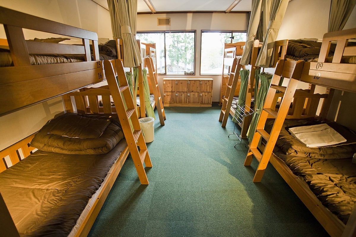 A dormitory room with bunk beds, a window, and a wooden cabinet.