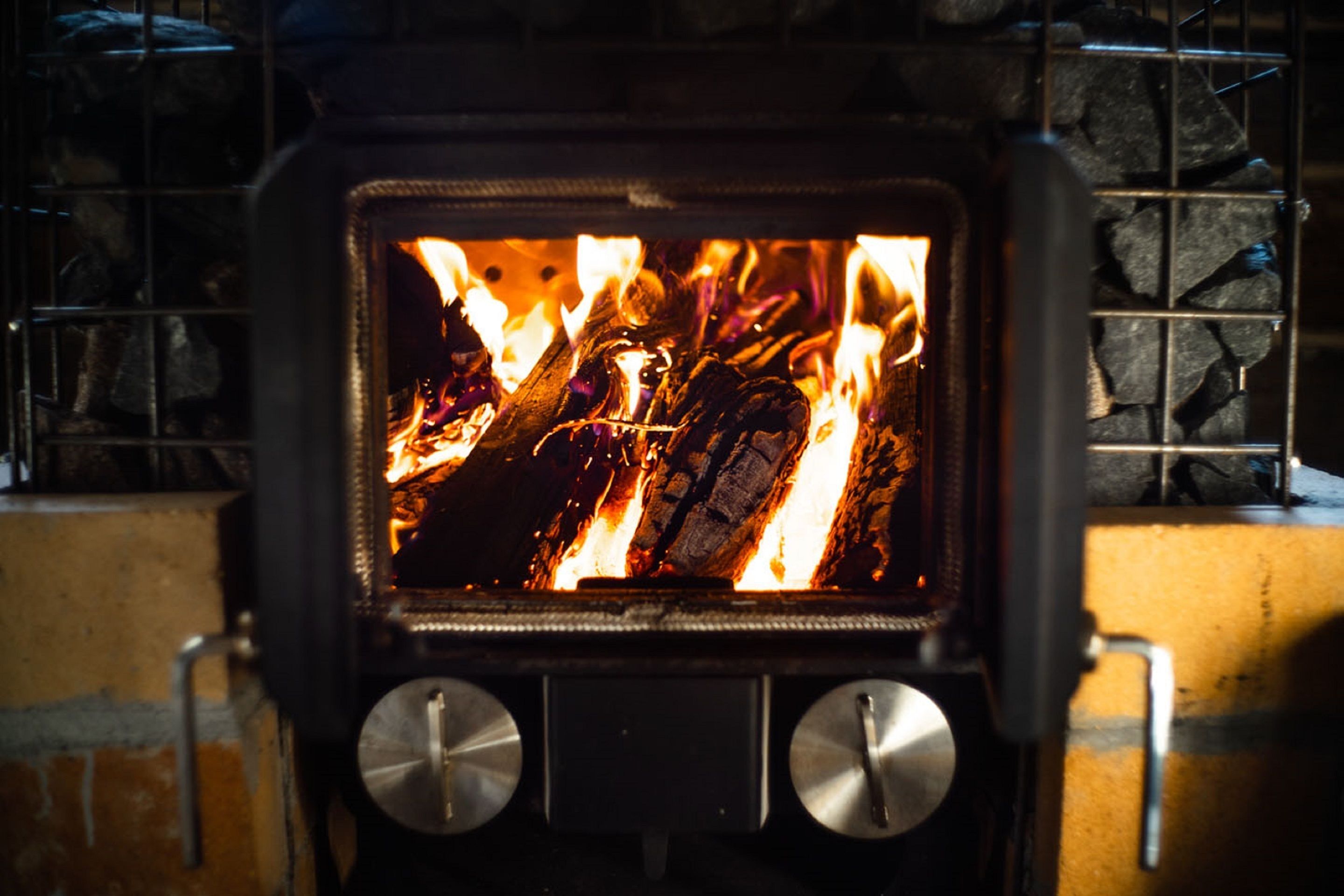 A wood-burning stove with a fire burning inside, surrounded by a stone wall.