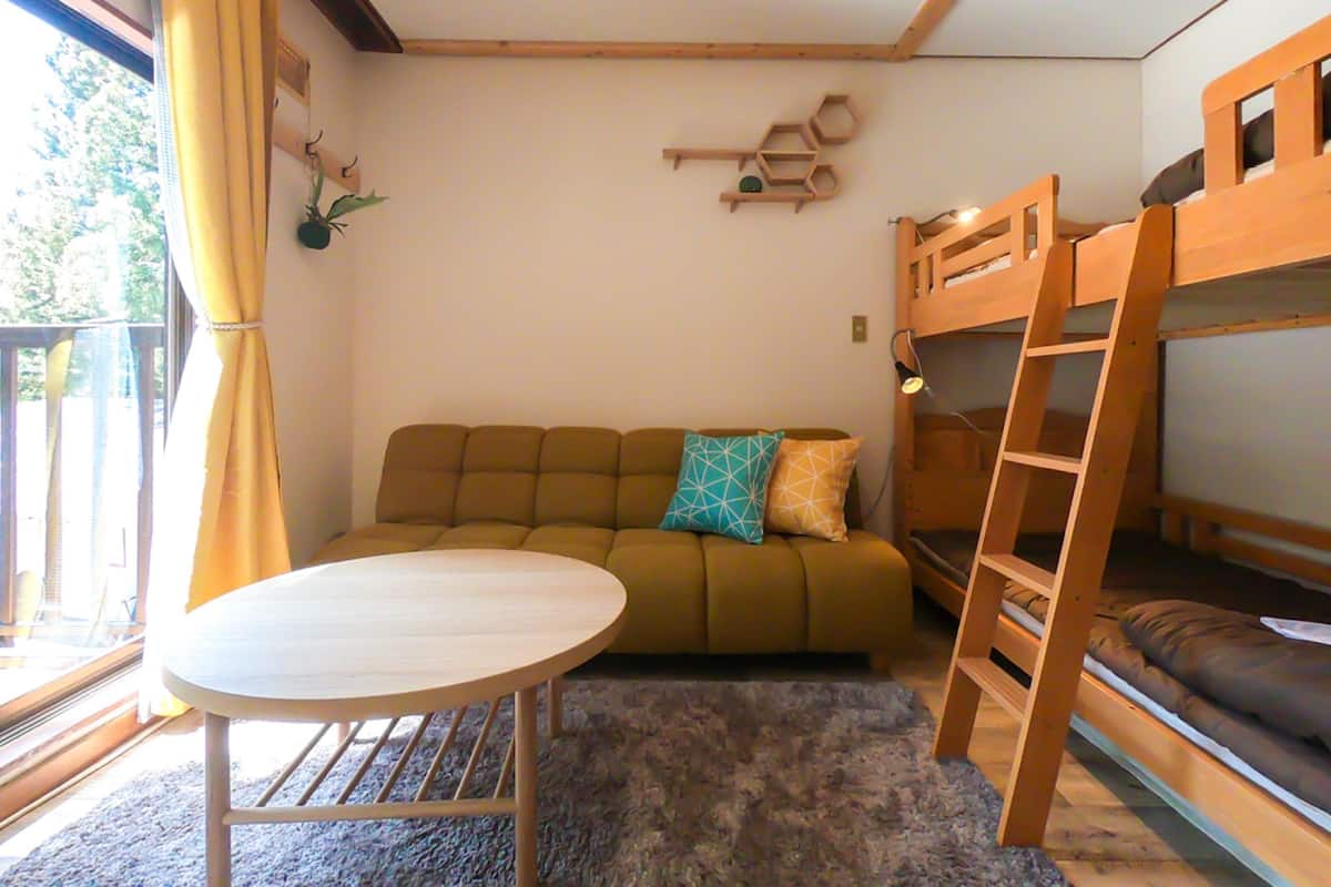 A room with a bunk bed, a sofa, a round table, and a window with curtains.