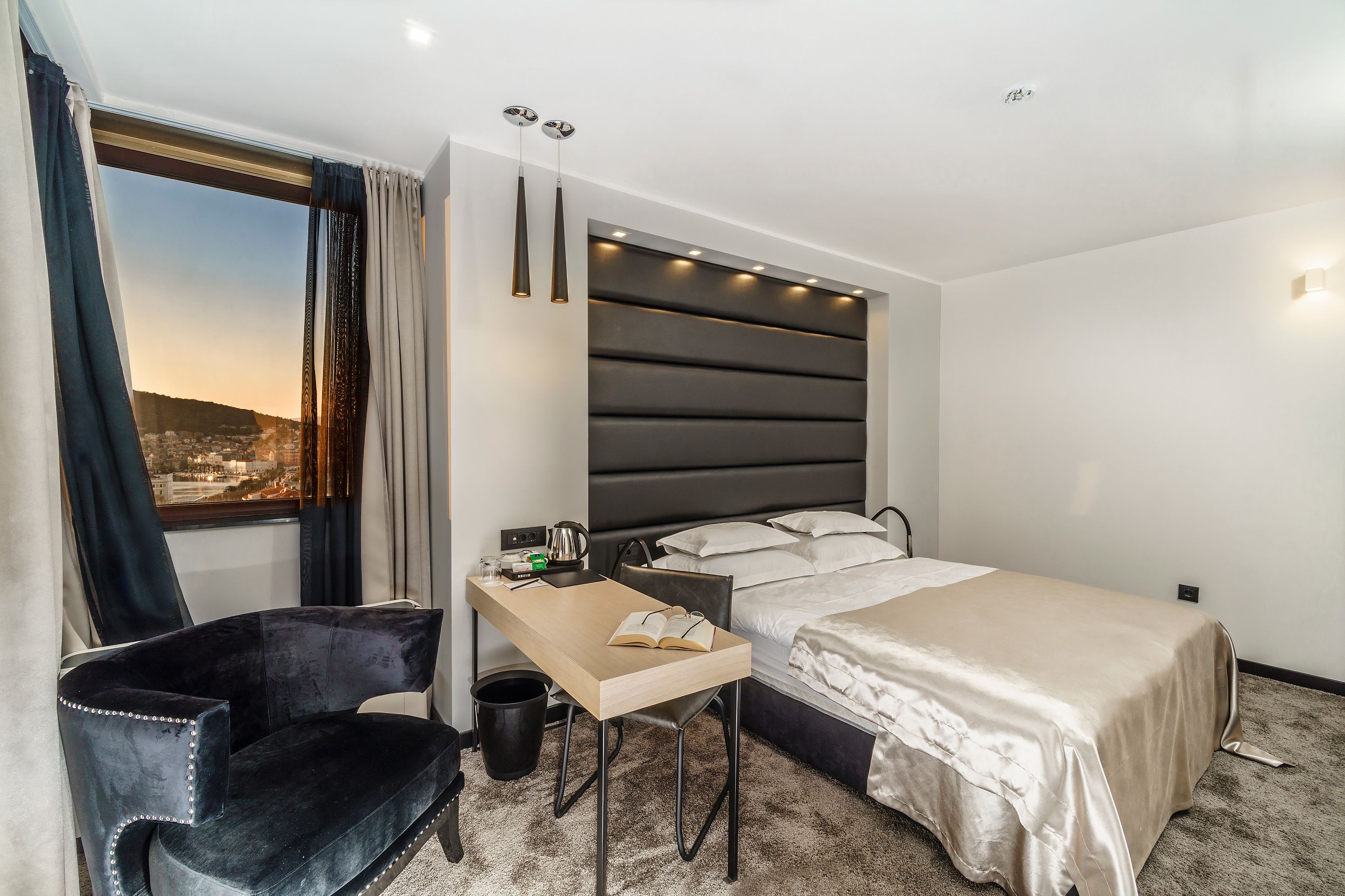 A hotel room with a bed, a desk, a chair, a window with curtains, and a city view.