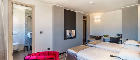 A modern hotel room with two beds, a red chair, a desk, and a bathroom visible through an open door.
