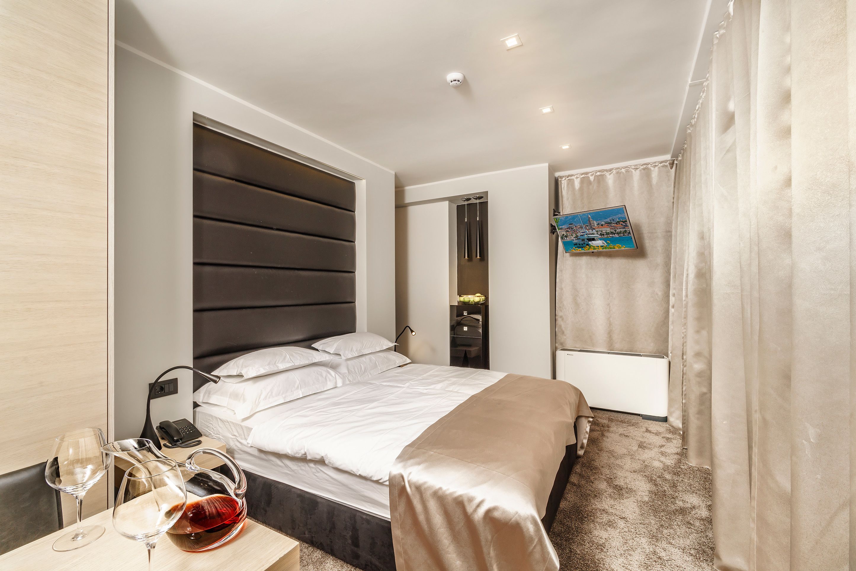 Camera d'albergo moderna con un letto grande, comodini con bicchieri da vino, un telefono e un quadro appeso al muro.