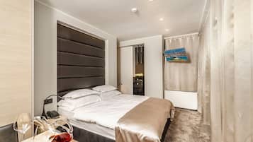 A modern hotel room with a large bed, bedside table with wine glasses, a telephone, and a painting on the wall.