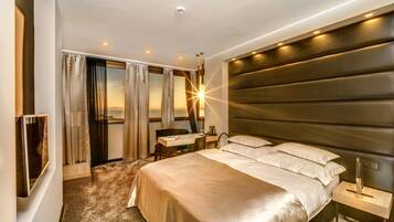 A hotel room with a large bed, a desk, and a view of the sunset through the window.