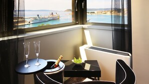 A corner room with a view of the sea, a small table with a bottle and glasses, and a piano. - The View Luxury Rooms (Split)