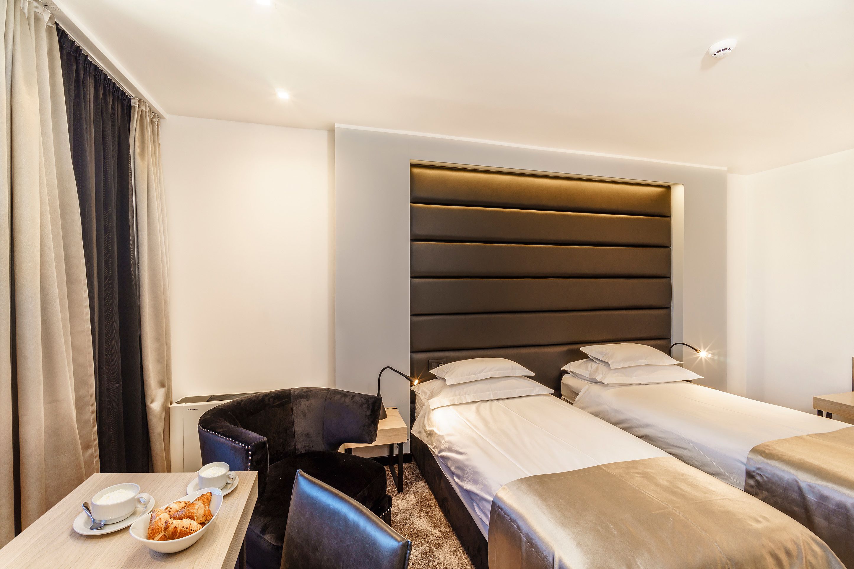 Une chambre d’hôtel avec deux lits simples, une petite table sur laquelle se trouvent un croissant, une tasse et une cuillère, ainsi qu’une chaise.