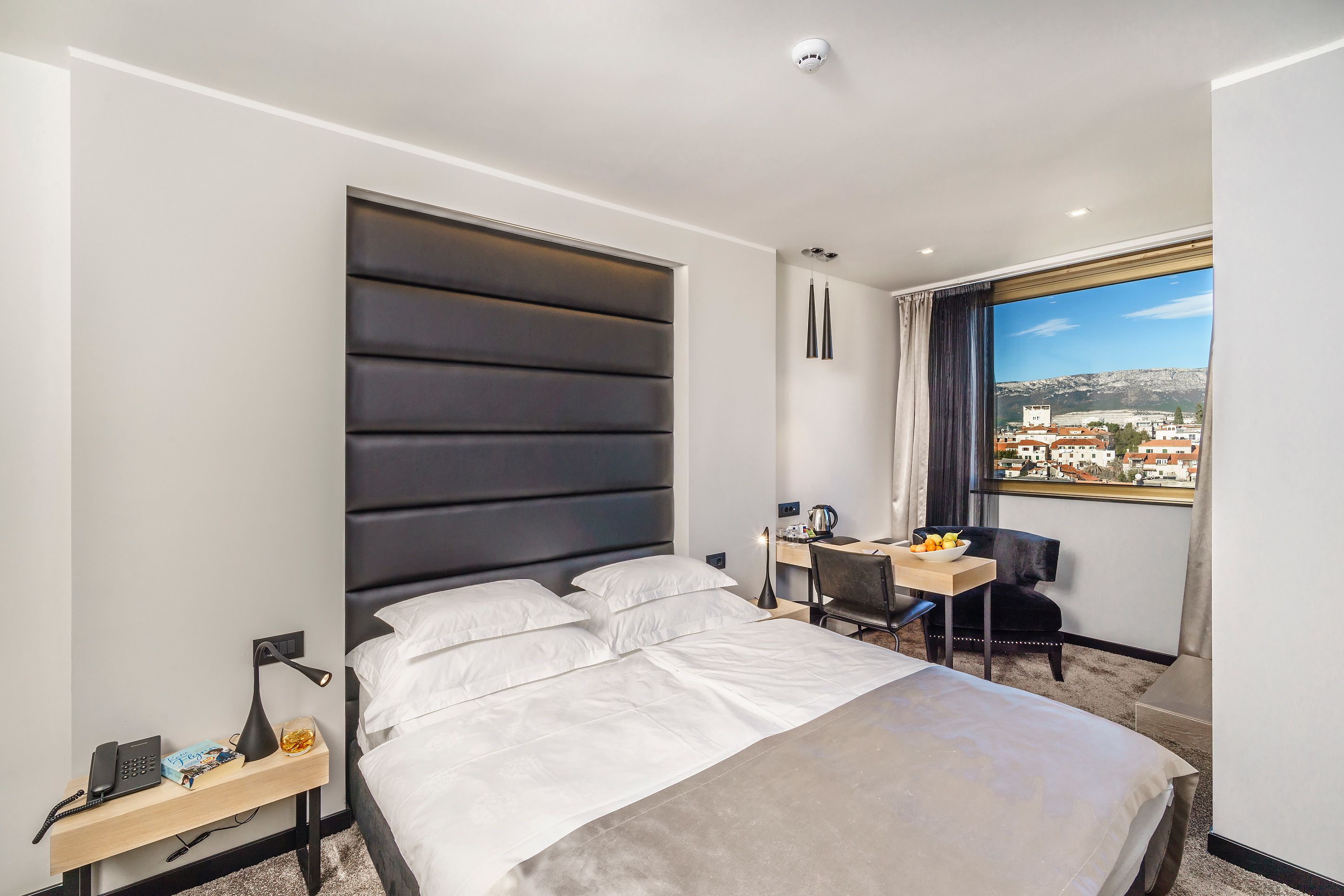 Een moderne hotelkamer met een groot bed, een bureau en uitzicht op een stadsgezicht.