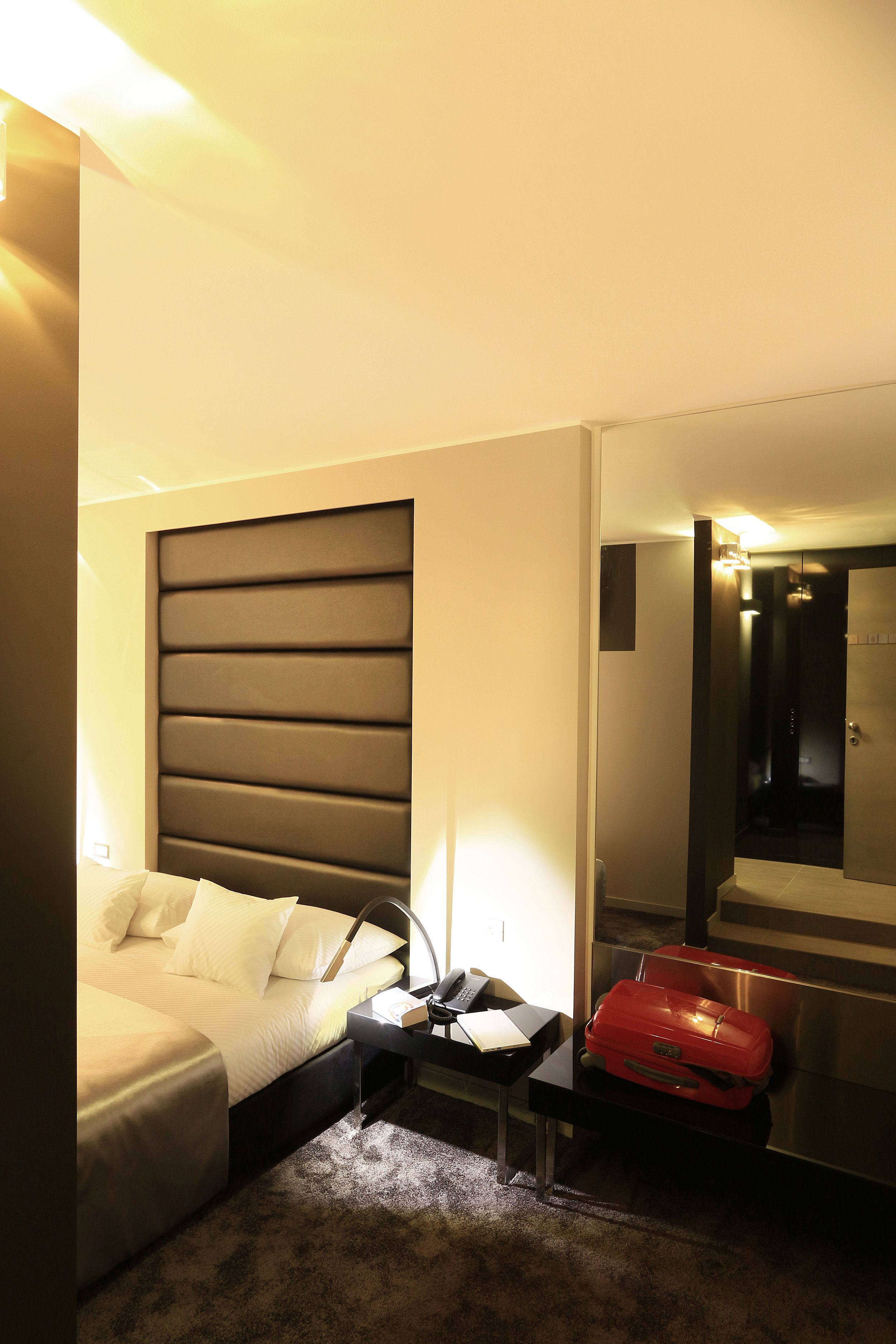 Een hotelkamer met een bed, nachtkastje en een rode koffer.