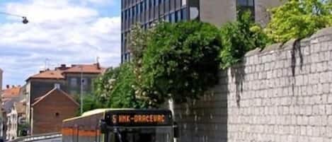 Un edificio alto de diseño moderno, un autobús con la leyenda "S WYK-DRACEUC" en la calle y un coche azul en el tráfico.