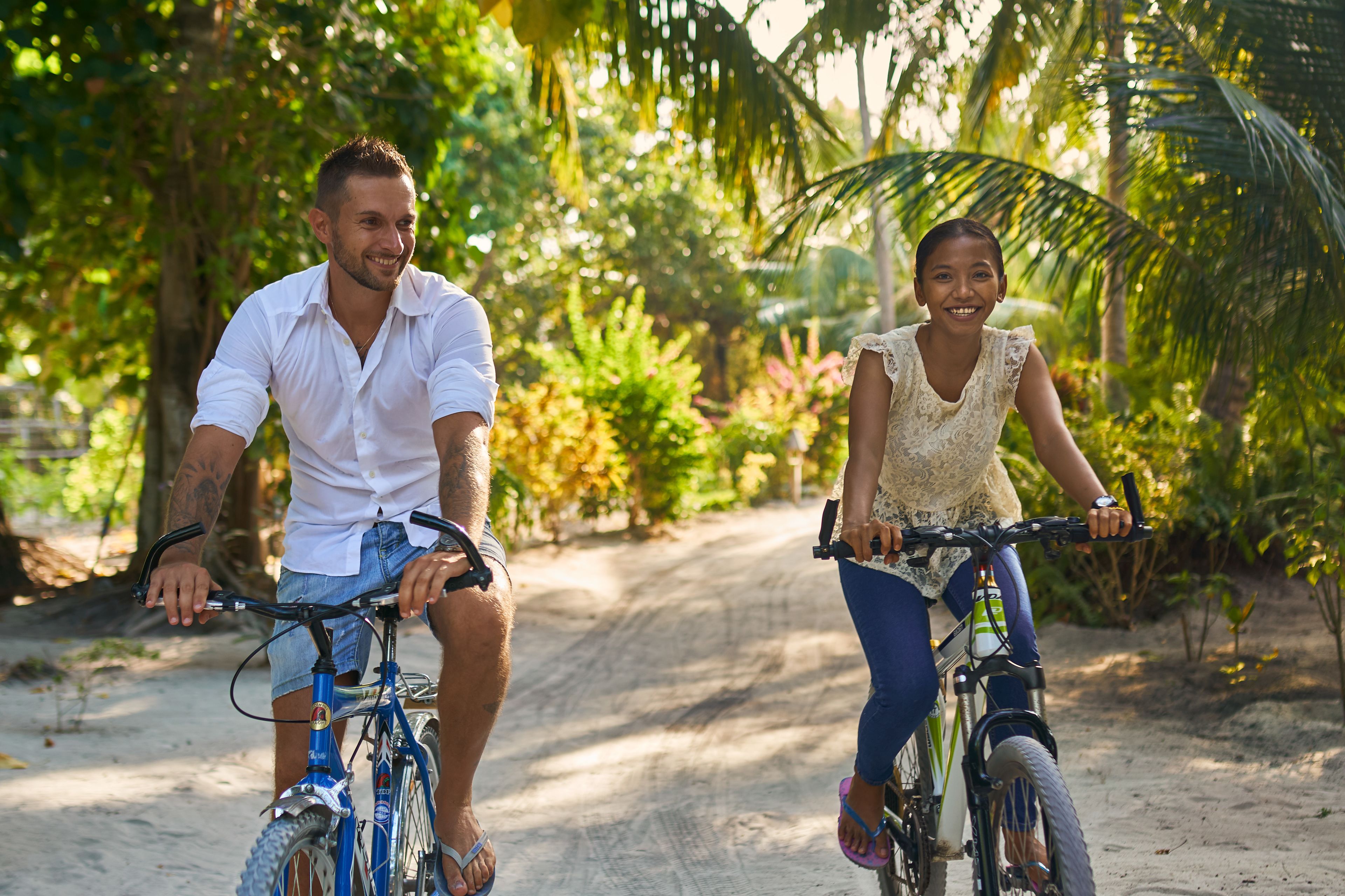 Two people riding bicycles on a dirt path surrounded by greenery.