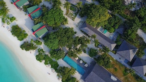 An aerial view of a resort with multiple bungalow-style accommodations, a central pool area, and lush greenery surrounding the buildings. - The Barefoot Eco Hotel (Hanimaadhoo)