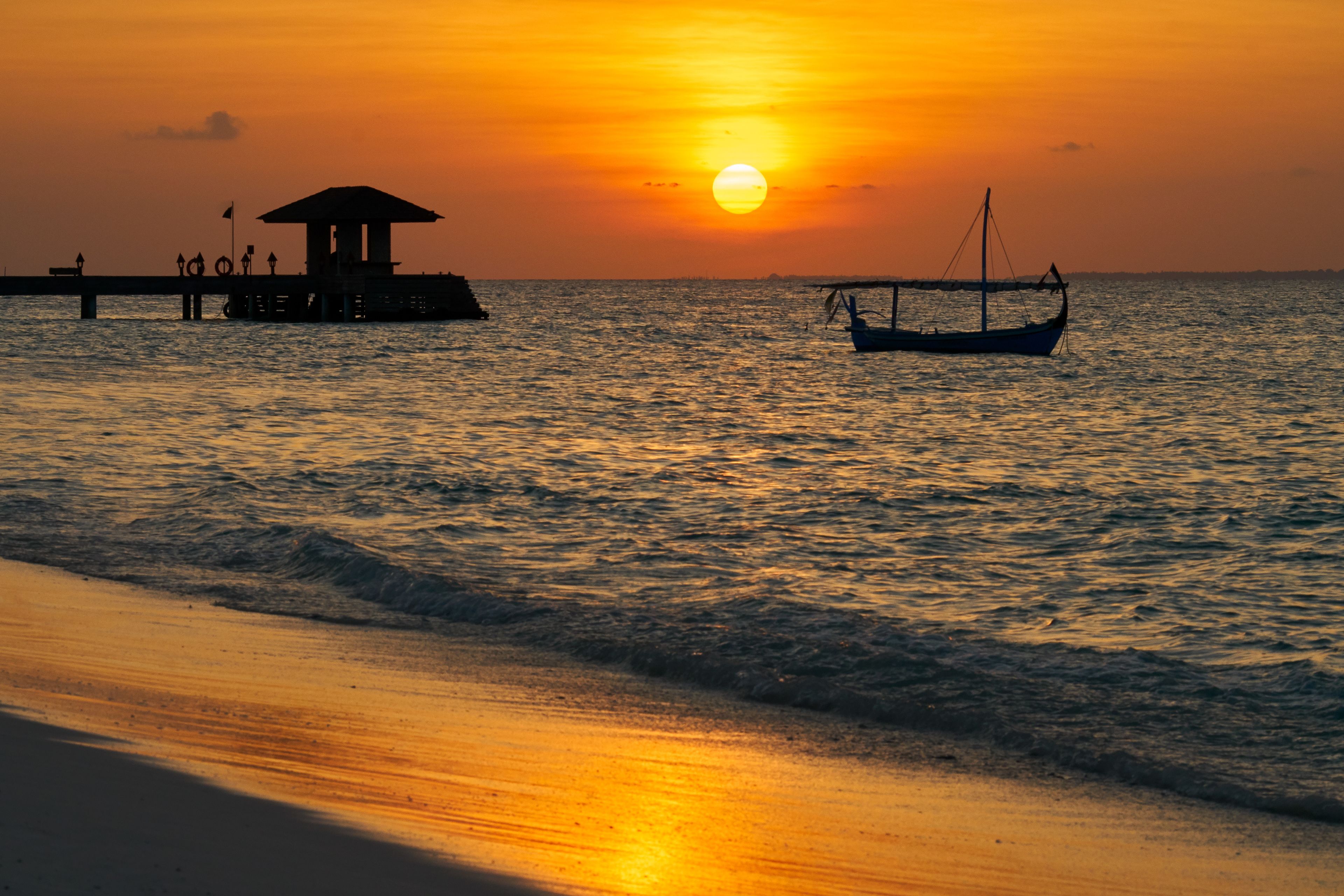 Un atardecer sobre una playa con un muelle y un barco.