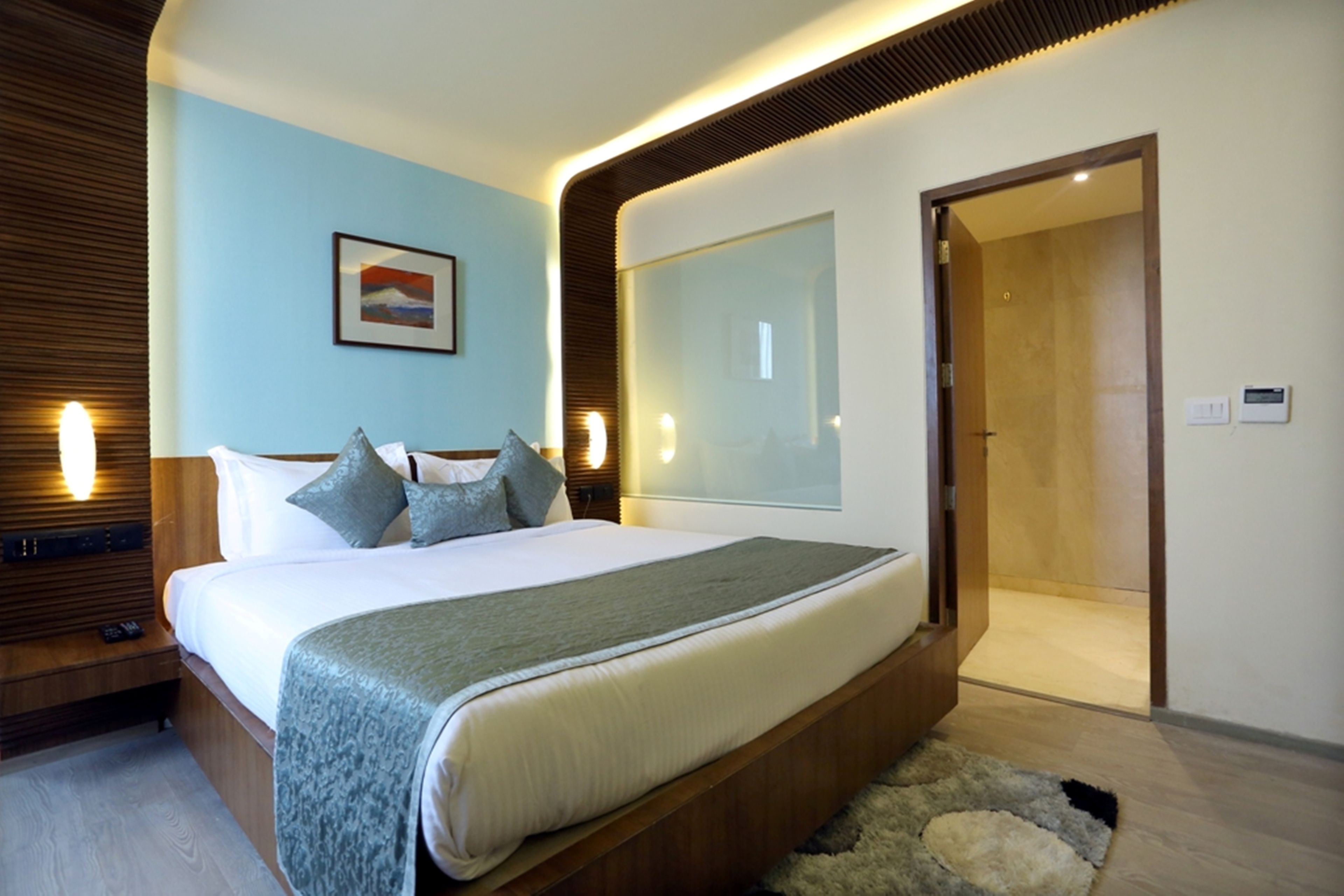 A modern bedroom with a large bed, wooden headboard, and a bedside table with a lamp.