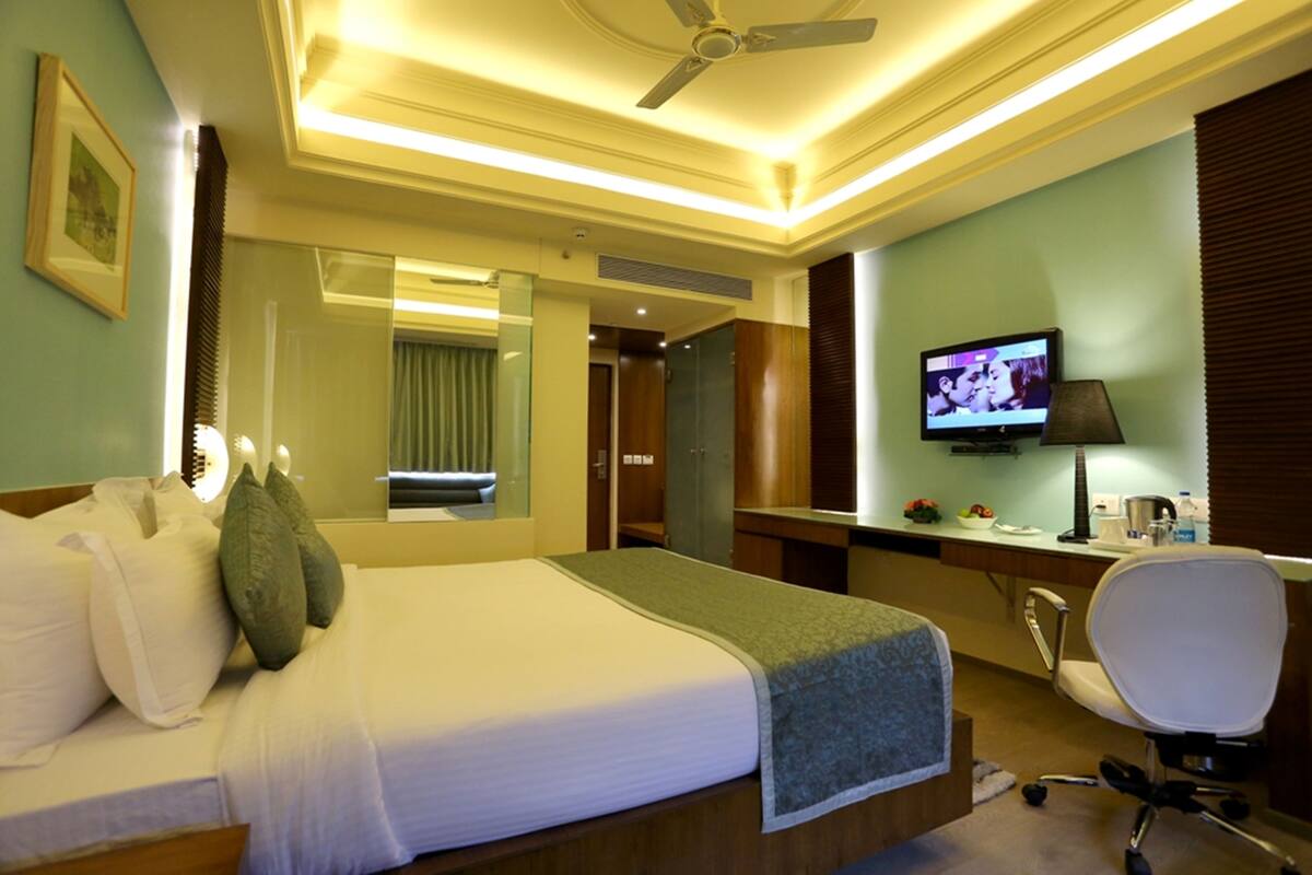 A hotel room with a bed, a desk, a television, and a ceiling fan.