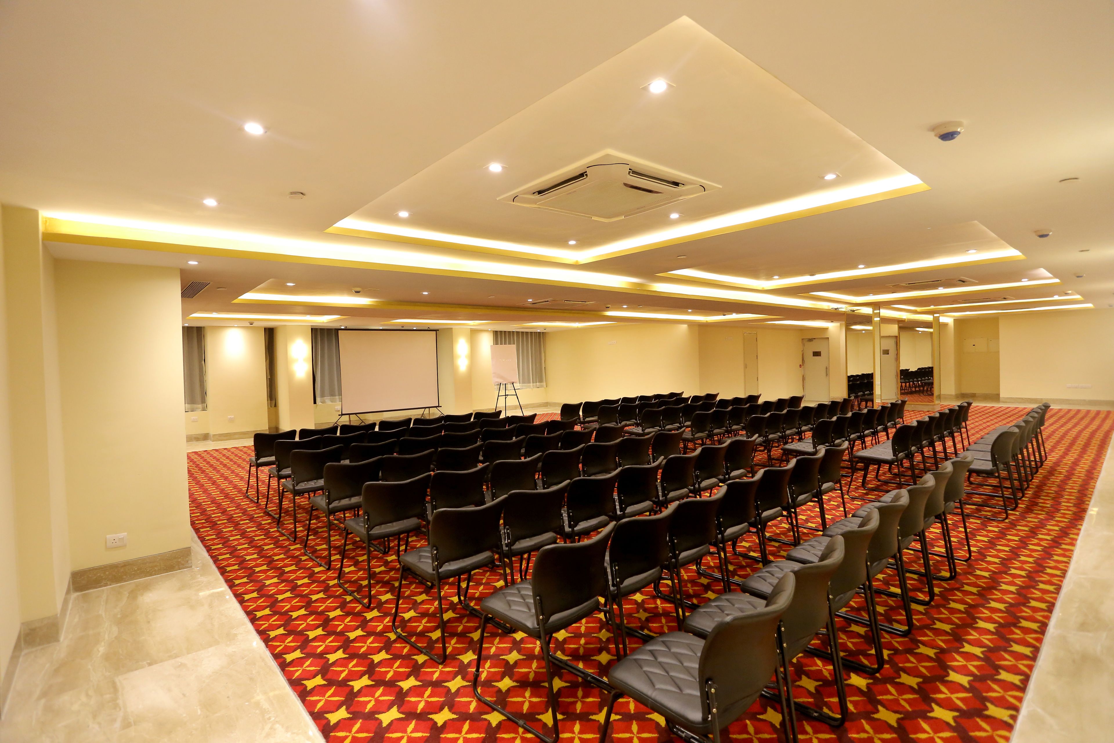 Un salón de conferencias con filas de sillas, una pantalla de proyector y piso alfombrado.