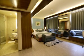 A modern bedroom with a large bed, a sofa, a mirror, and a bathroom with a toilet and sink. - Regenta Orko's Kolkata (Kolkata)