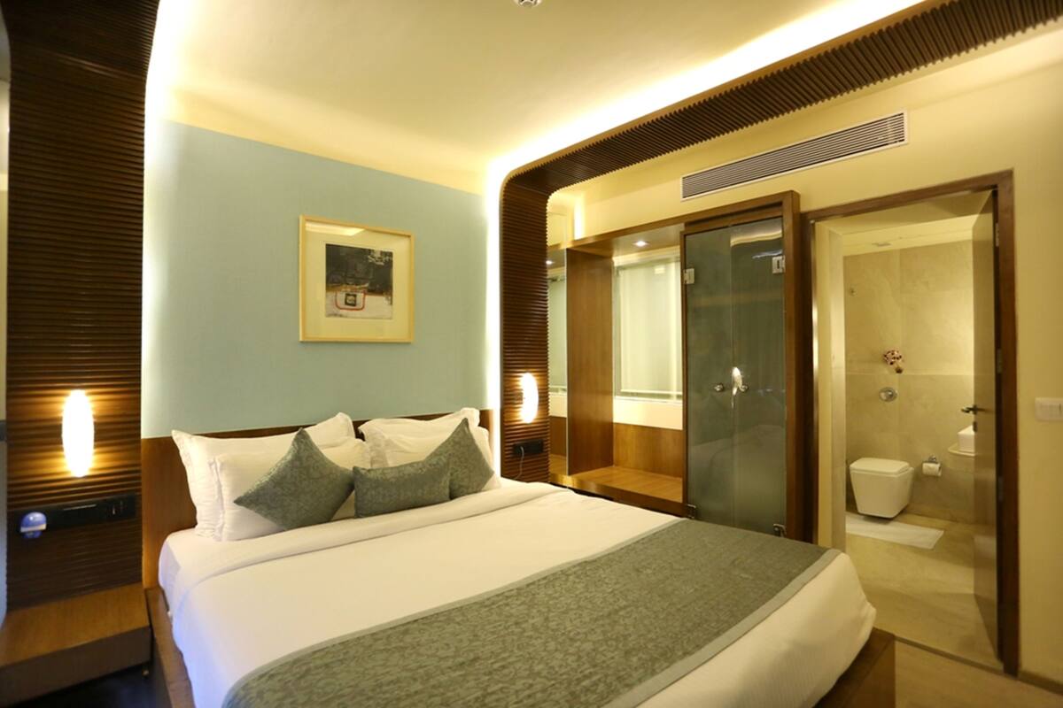 A hotel room with a large bed, a bedside table, a mirror, and a bathroom with a shower and toilet.