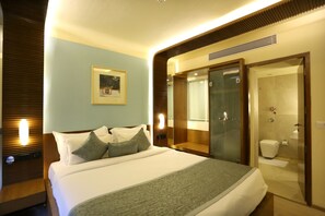 Ein Hotelzimmer mit einem großen Bett, einem Nachttisch, einem Spiegel und einem Badezimmer mit Dusche und Toilette.
