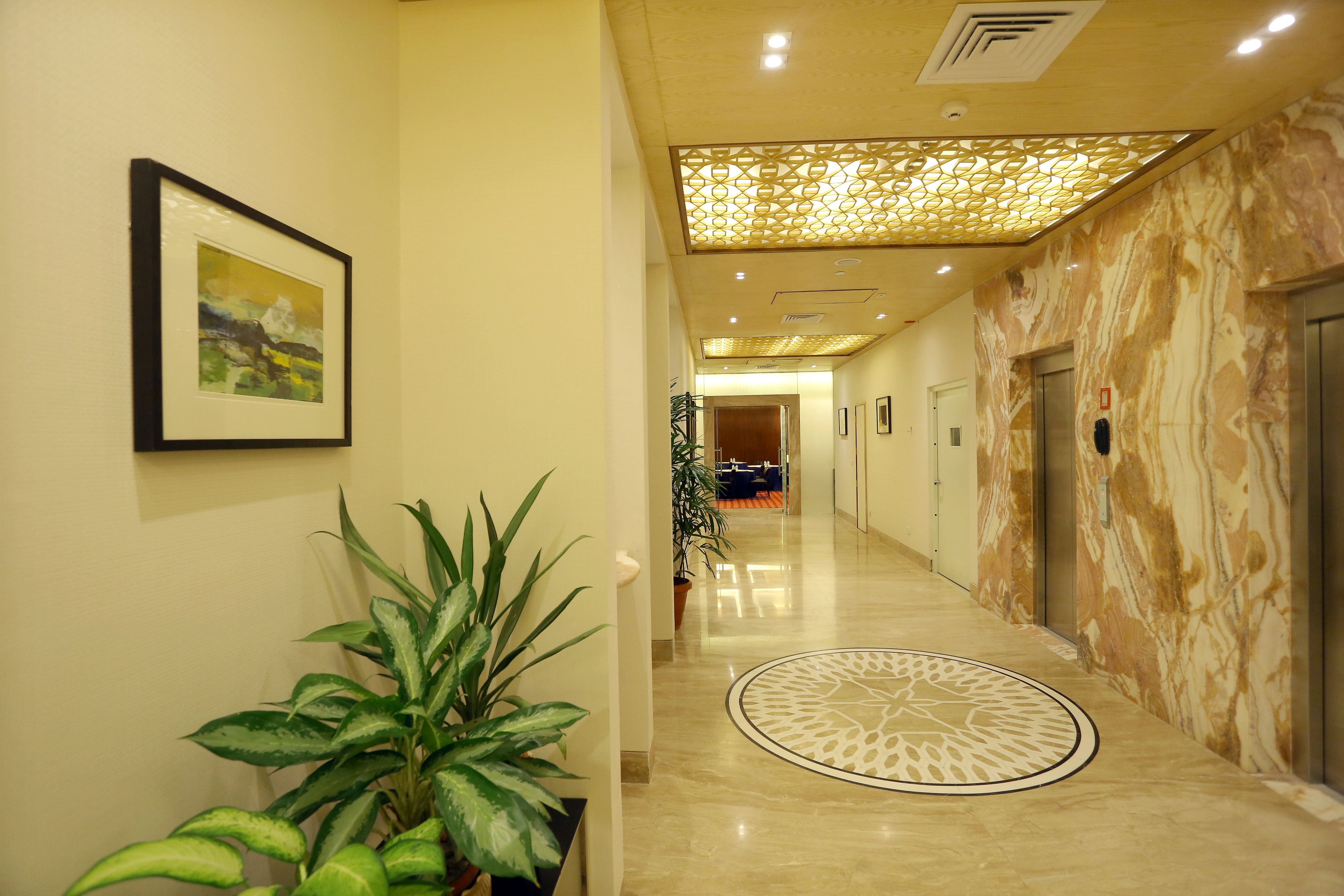 A hotel corridor with a marble floor, a patterned ceiling, and a framed picture on the wall.