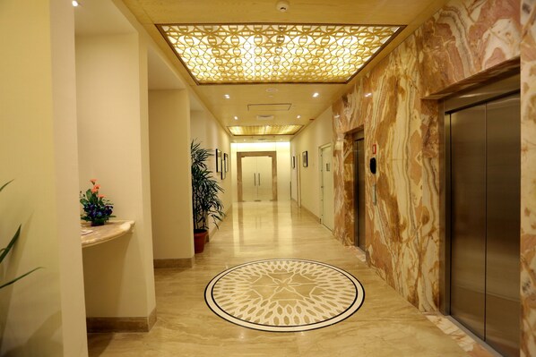 A hotel corridor with a marble floor, a decorative ceiling, and an elevator.
